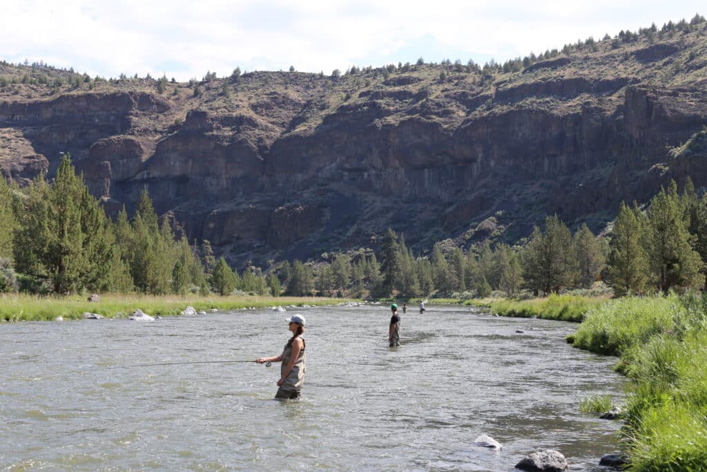 Two anglers stand waist deep in the Crooked River with it's scenic canyon in the background. With vast amounts of wading access, these anglers are enjoying this stronghold of native rainbow trout and whitefish located just east of Bend, OR.