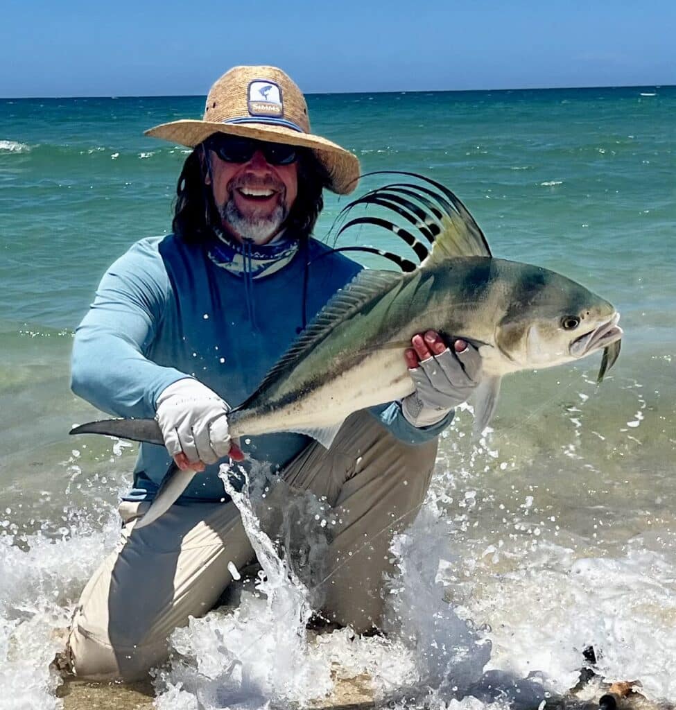 An angler kneeling while holding a Mexican Roosterfish